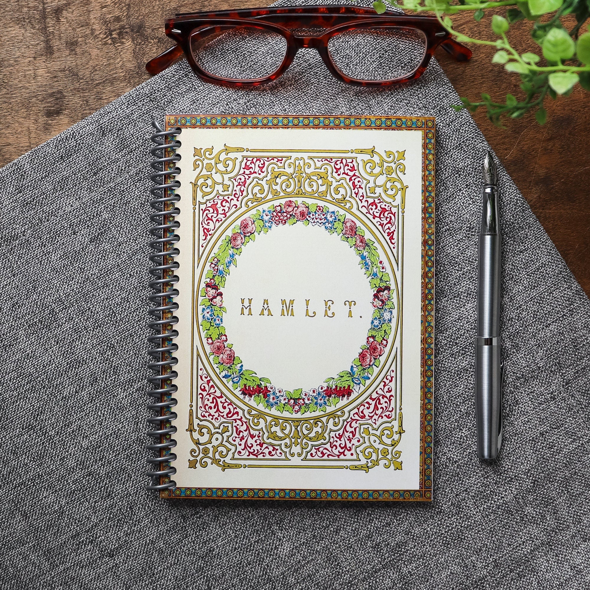 Handmade travel notebook (5 x 7 inches) featuring cover of a vintage copy of Hamlet by William Shakespeare. Colors: bronze and jewel tones- green red, gold, blue. Floral Patterns and intricate frame.