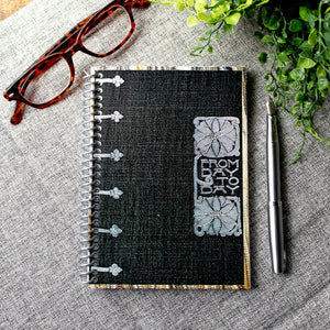 A travel-sized spiral notebook featuring a vintage book cover: FromDay To Day. Features a bold floral design. The colors are black, silver, gold and brown.