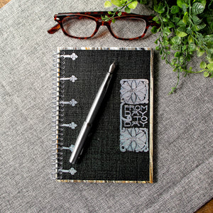 A travel-sized spiral notebook featuring a vintage book cover: FromDay To Day. Features a bold floral design. The colors are black, silver, gold and brown.