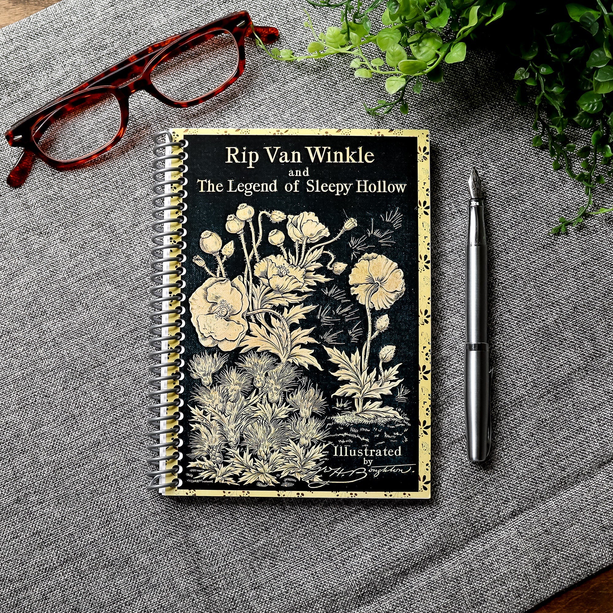 A travel-sized spiral notebook featuring a vintage book cover: Rip Van Winkle and The Legend of Sleepy Hollow by Washington Irving. Features a bold floral design. The colors are black and gold.