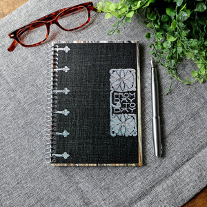 A travel-sized spiral notebook featuring a vintage book cover: FromDay To Day. Features a bold floral design. The colors are black, silver, gold and brown.